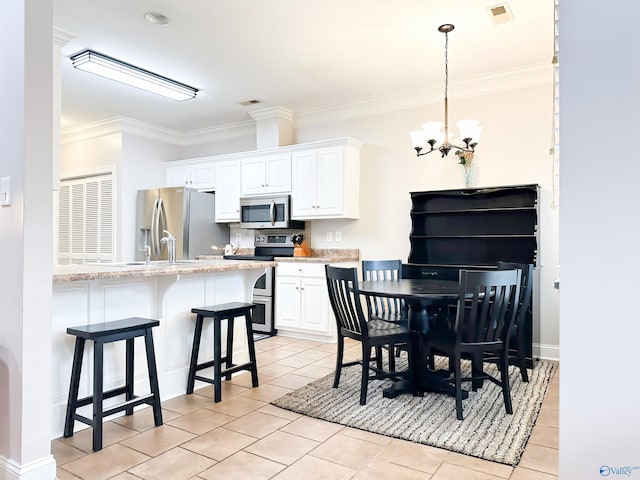 kitchen with crown molding, a kitchen breakfast bar, stainless steel appliances, an inviting chandelier, and white cabinetry