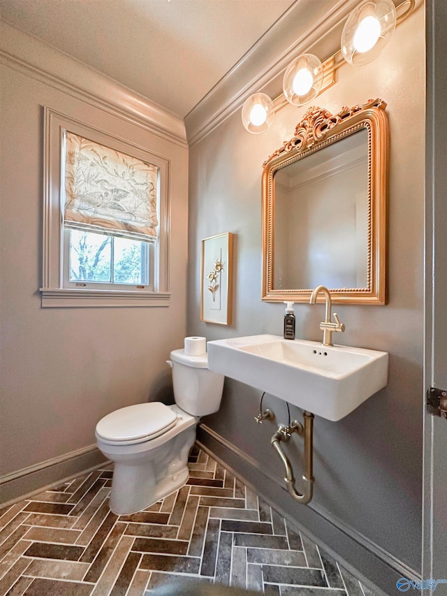 bathroom featuring a sink, brick floor, baseboards, toilet, and ornamental molding
