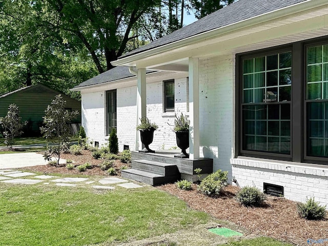 property entrance with roof with shingles, crawl space, covered porch, a lawn, and brick siding