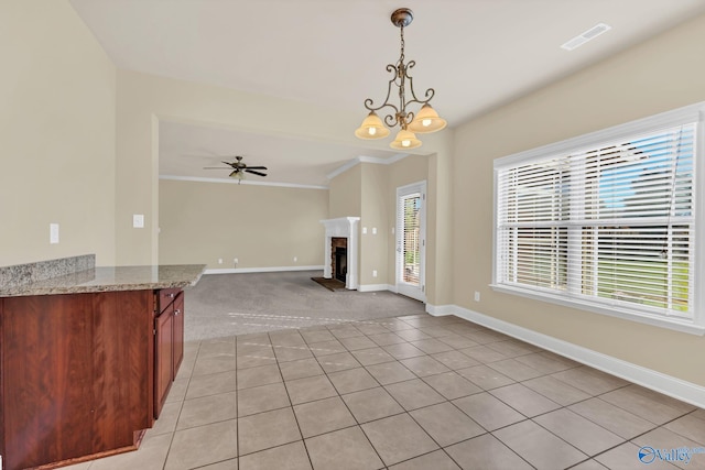 kitchen featuring light stone counters, hanging light fixtures, ornamental molding, light tile patterned floors, and ceiling fan with notable chandelier