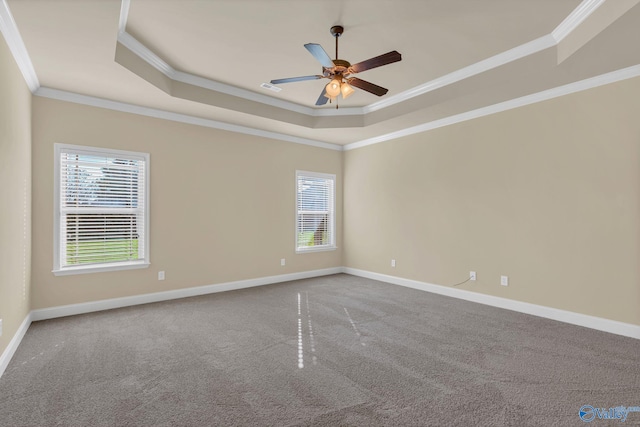 carpeted empty room featuring a raised ceiling, ceiling fan, crown molding, and a healthy amount of sunlight