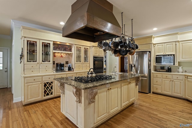 kitchen featuring island exhaust hood, cream cabinetry, a center island with sink, and black appliances