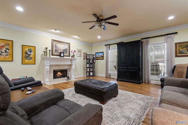 living room with ceiling fan, ornamental molding, a fireplace, and light wood-type flooring