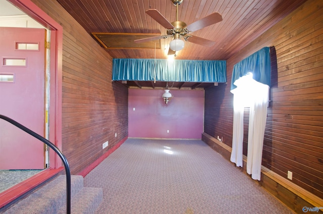 carpeted spare room with wooden ceiling, wood walls, baseboards, and ceiling fan