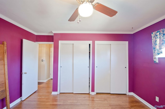 unfurnished bedroom with crown molding, light wood-style flooring, baseboards, and two closets