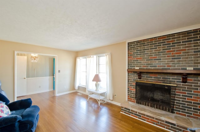 living area with a fireplace, a textured ceiling, baseboards, and wood finished floors