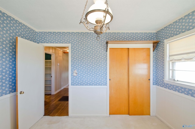 bedroom with wallpapered walls, a closet, ornamental molding, and a wainscoted wall