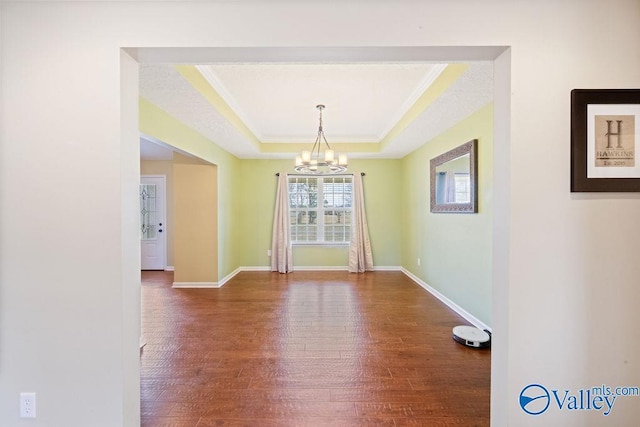 unfurnished dining area with a chandelier, a tray ceiling, baseboards, and wood finished floors