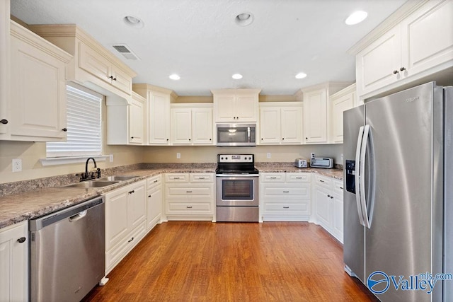 kitchen with light wood finished floors, stainless steel appliances, recessed lighting, visible vents, and a sink