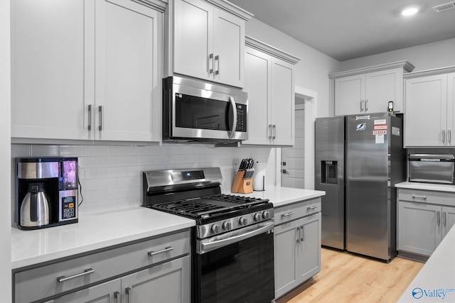 kitchen featuring stainless steel appliances, light hardwood / wood-style floors, decorative backsplash, and gray cabinetry