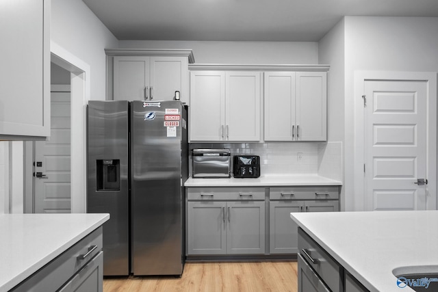 kitchen with gray cabinetry, backsplash, light hardwood / wood-style floors, and stainless steel refrigerator with ice dispenser