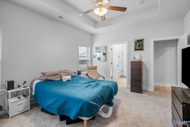 bedroom featuring ceiling fan, connected bathroom, a raised ceiling, and light colored carpet