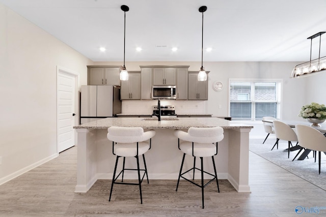 103 Barlow Way, Owens Cross Roads, AL 35763 - kitchen featuring appliances with stainless steel finishes, gray cabinets, an island with sink, a breakfast bar, and tasteful backsplash