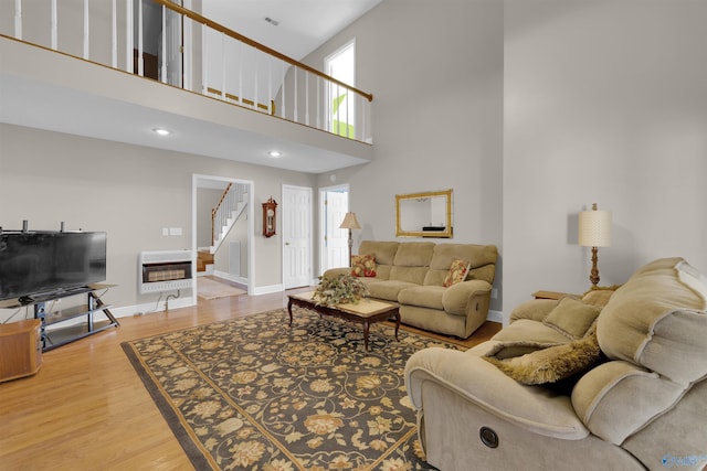 living room with heating unit, wood-type flooring, a towering ceiling, and plenty of natural light