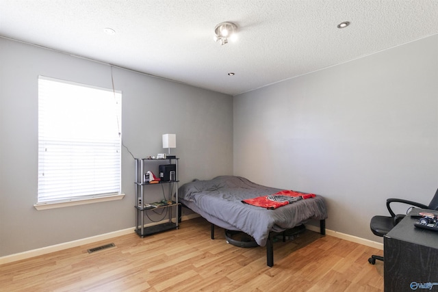 bedroom with baseboards, visible vents, light wood finished floors, and a textured ceiling