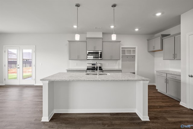 kitchen featuring light stone countertops, appliances with stainless steel finishes, a center island with sink, gray cabinets, and hanging light fixtures