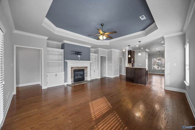 unfurnished living room with dark wood-type flooring, a raised ceiling, a stone fireplace, and ceiling fan with notable chandelier