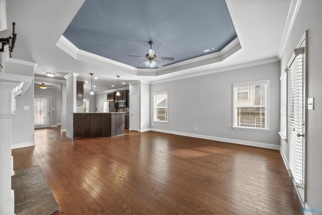 unfurnished living room with plenty of natural light, a raised ceiling, ceiling fan, and dark wood-style flooring