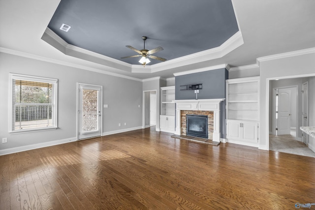 unfurnished living room with a ceiling fan, a raised ceiling, a fireplace, and wood finished floors