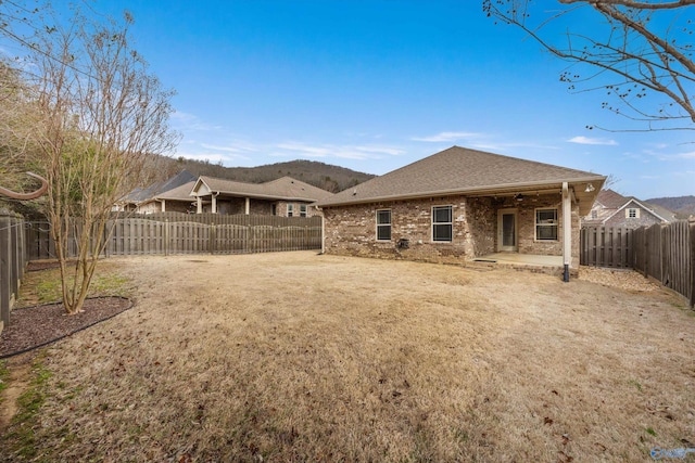 back of house featuring a fenced backyard, brick siding, a shingled roof, a yard, and a patio area