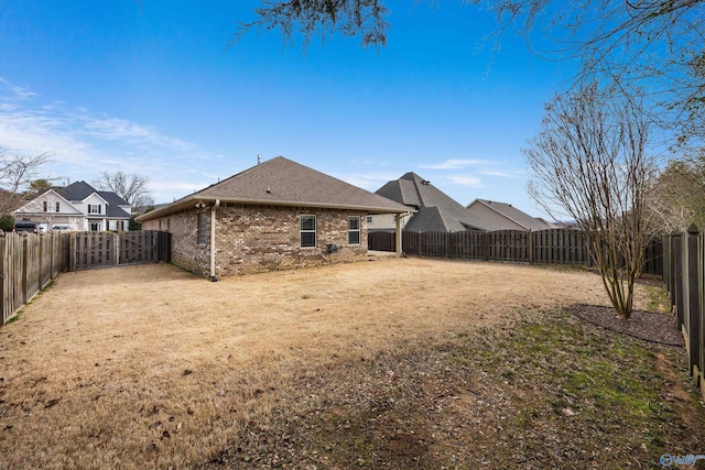 rear view of house with a yard, a fenced backyard, roof with shingles, and brick siding