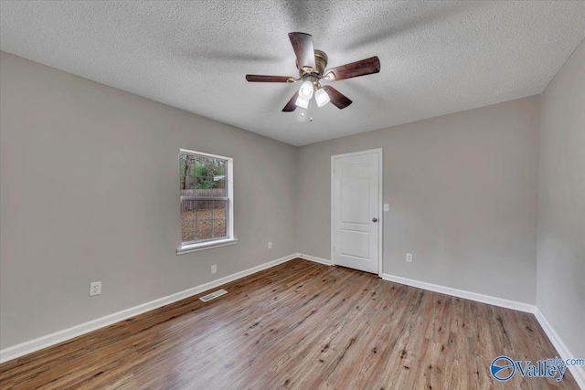 spare room featuring a textured ceiling, visible vents, baseboards, wood finished floors, and a ceiling fan