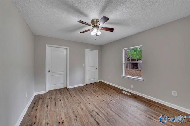 unfurnished bedroom with visible vents, a textured ceiling, baseboards, and wood finished floors