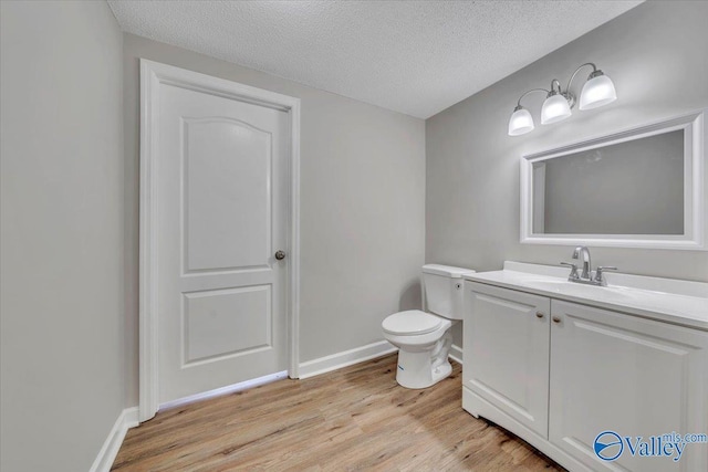 half bath with toilet, vanity, wood finished floors, a textured ceiling, and baseboards