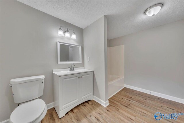 bathroom featuring vanity, toilet, baseboards, a textured ceiling, and wood finished floors