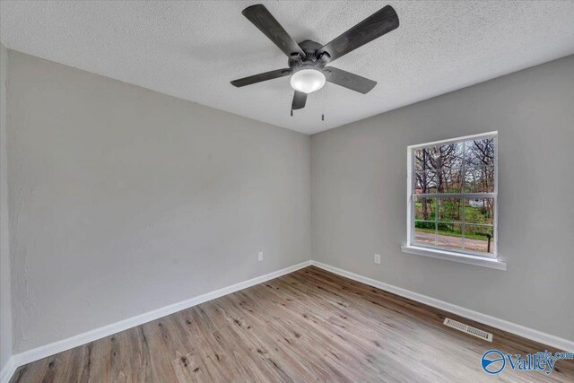 spare room with baseboards, a textured ceiling, visible vents, and wood finished floors