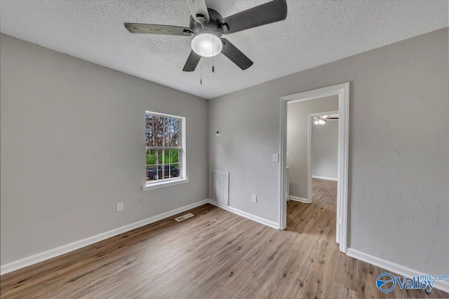unfurnished bedroom with wood finished floors, a textured ceiling, baseboards, and visible vents