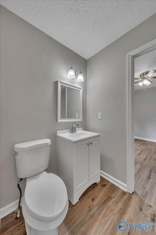 half bath with vanity, toilet, baseboards, a textured ceiling, and wood finished floors