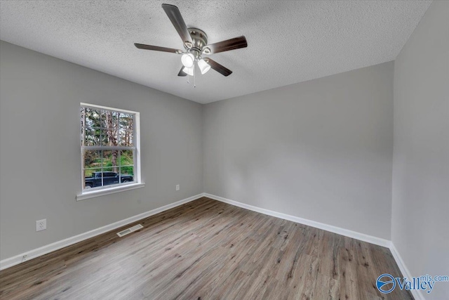 spare room featuring a textured ceiling, baseboards, wood finished floors, and a ceiling fan