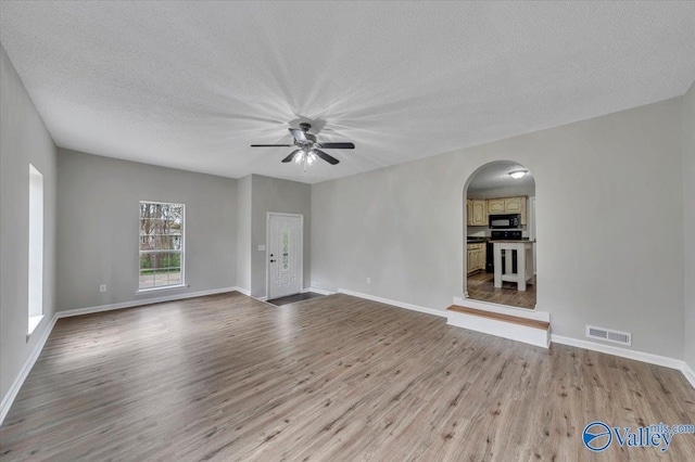 unfurnished living room with visible vents, wood finished floors, arched walkways, and a ceiling fan