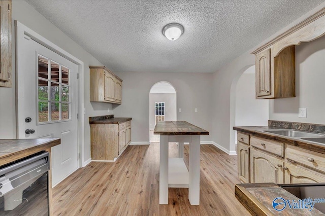 kitchen with light wood finished floors, dark countertops, arched walkways, and wine cooler