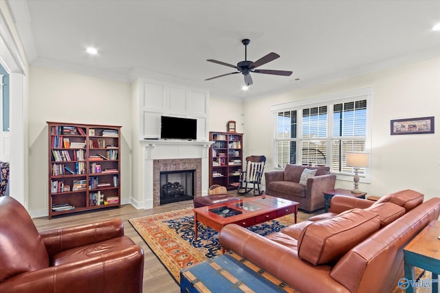 living room with ceiling fan, ornamental molding, a fireplace, and light wood-type flooring