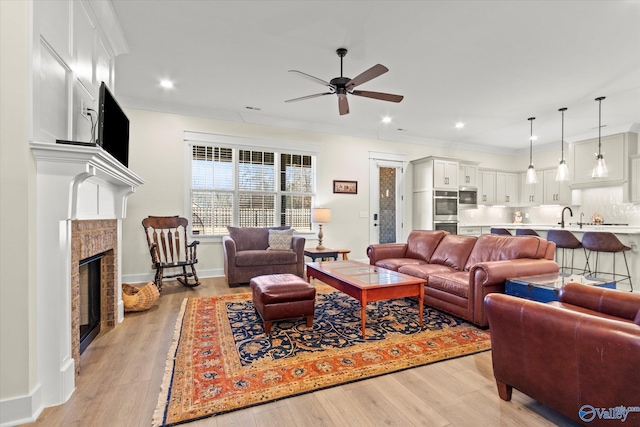 living room with sink, light hardwood / wood-style flooring, ornamental molding, ceiling fan, and a tiled fireplace