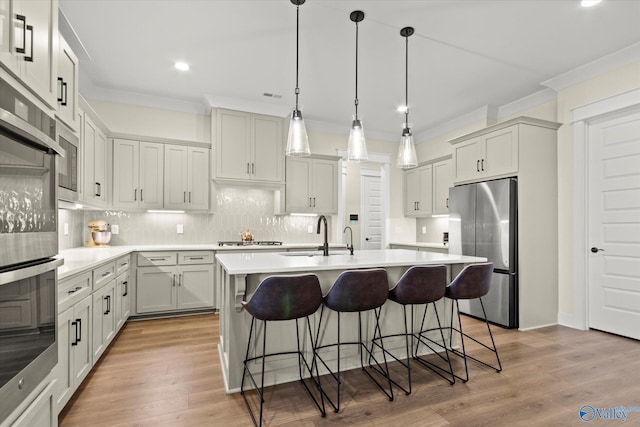 kitchen featuring pendant lighting, sink, a kitchen island with sink, and stainless steel refrigerator