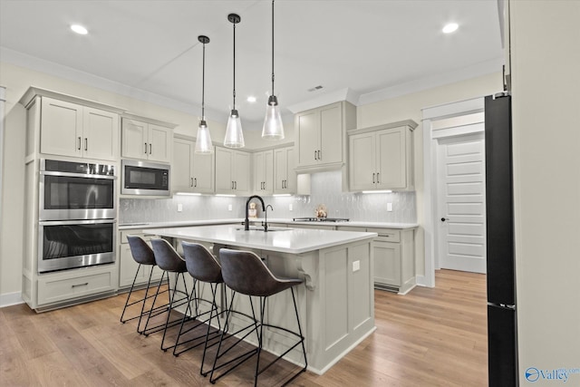 kitchen with sink, a breakfast bar area, stainless steel appliances, a center island with sink, and light wood-type flooring