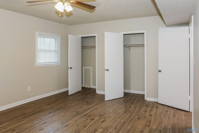 unfurnished bedroom with two closets, ceiling fan, dark wood-type flooring, and a textured ceiling