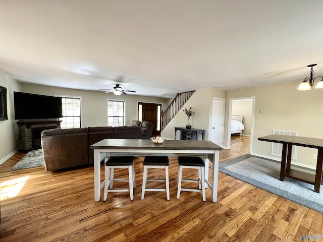 dining area with light wood-style floors, ceiling fan with notable chandelier, visible vents, stairs, and baseboards