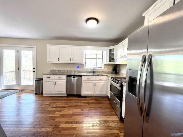 kitchen with light stone counters, white cabinets, dark wood-type flooring, appliances with stainless steel finishes, and a sink