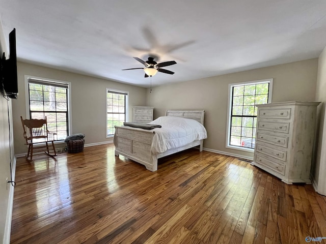 bedroom featuring a ceiling fan, wood-type flooring, multiple windows, and baseboards
