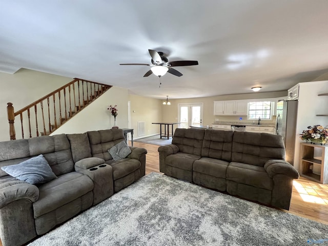 living area featuring visible vents, light wood-style flooring, ceiling fan, and stairs