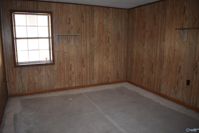 spare room featuring unfinished concrete floors, wooden walls, and baseboards