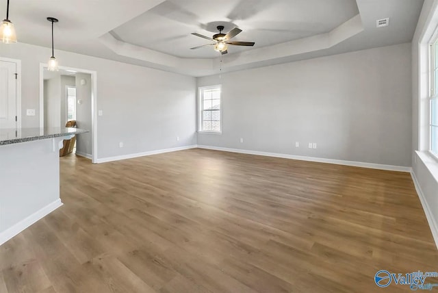 unfurnished living room with ceiling fan, a raised ceiling, and wood-type flooring