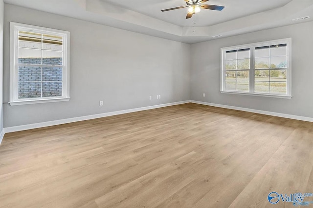 spare room featuring a raised ceiling, ceiling fan, and light hardwood / wood-style floors