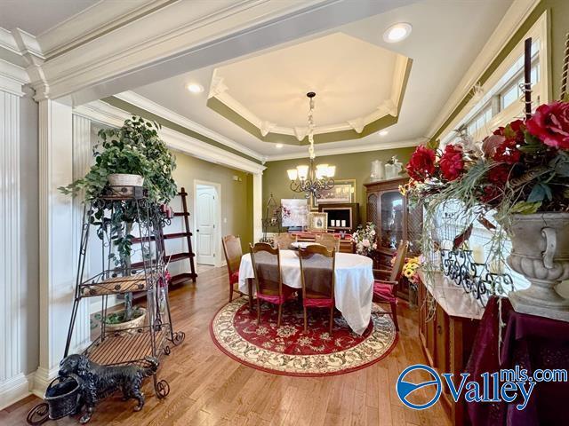 dining area featuring decorative columns, a tray ceiling, crown molding, a chandelier, and hardwood / wood-style floors