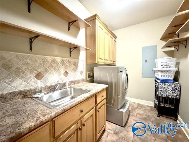 clothes washing area featuring cabinets, hookup for a washing machine, electric panel, and sink