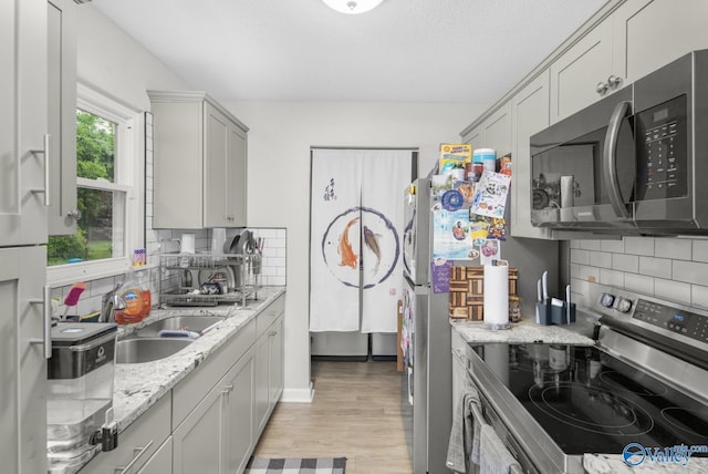 kitchen featuring a sink, light wood-style floors, decorative backsplash, light stone counters, and appliances with stainless steel finishes